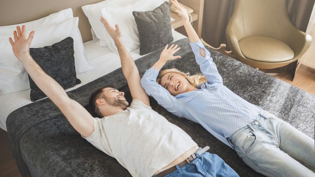 A joyful couple lying on a bed with their arms raised and laughing.