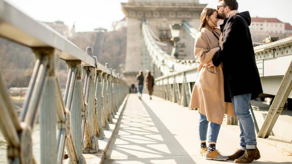 A couple sharing a kiss while standing together on a bridge.