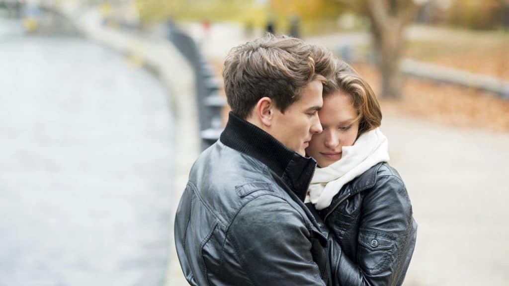 A couple wearing leather jackets embracing closely by the water.