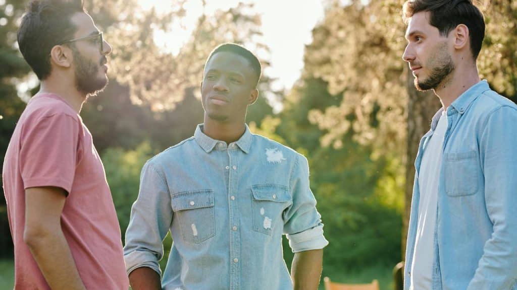 A group of three men standing outdoors having a conversation.