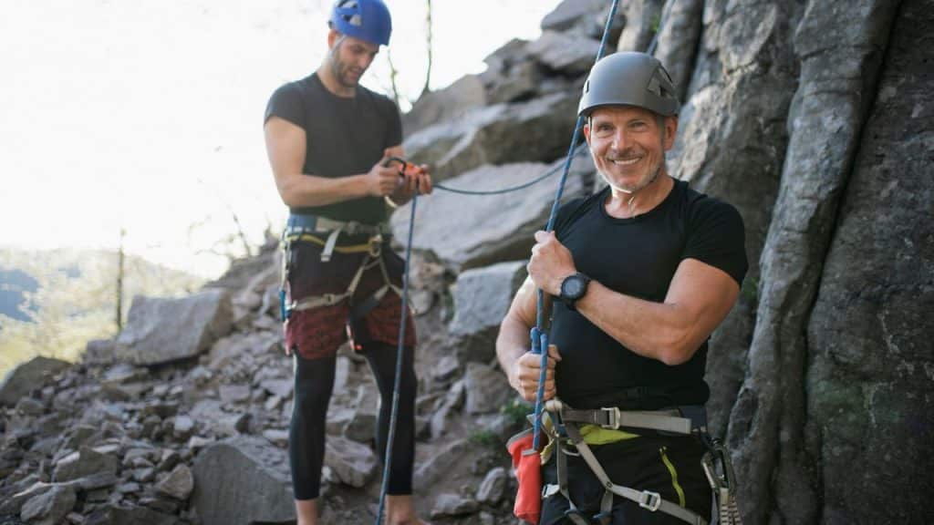 Two men in climbing harnesses and helmets are on a rocky outcrop.