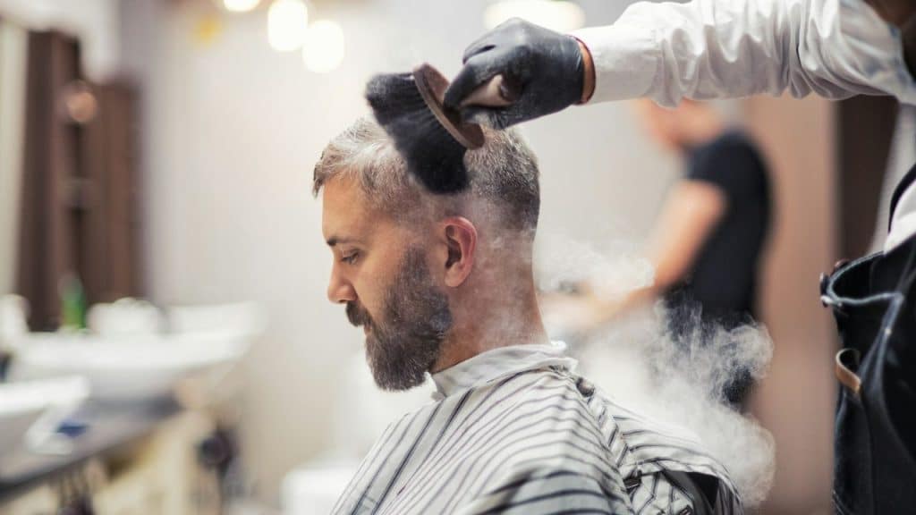 A barber brushes the neck of a man sitting in a barber's chair.