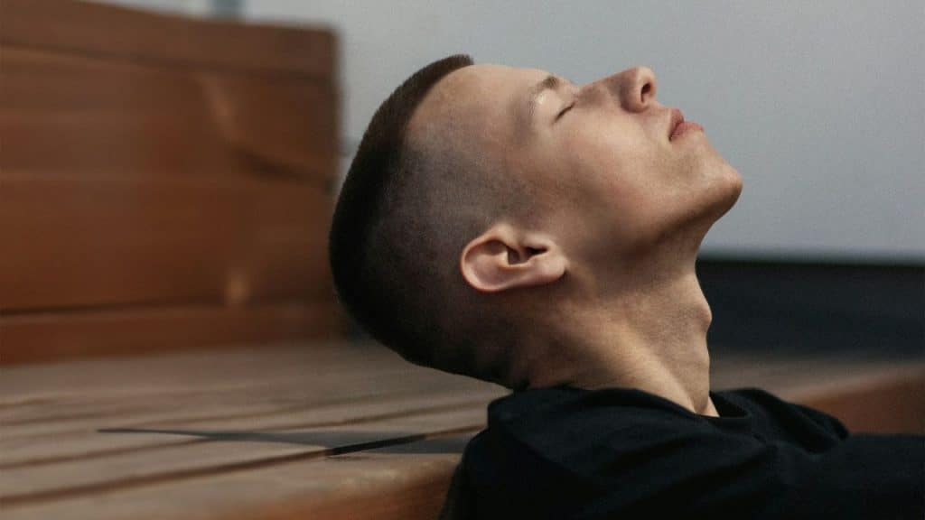 A man with his head tilted back and eyes closed leans against a wooden surface.