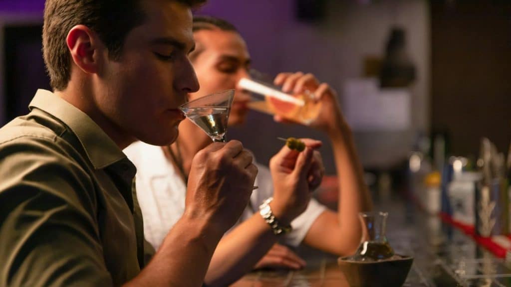 Two men are drinking at a bar, seen from the side.
