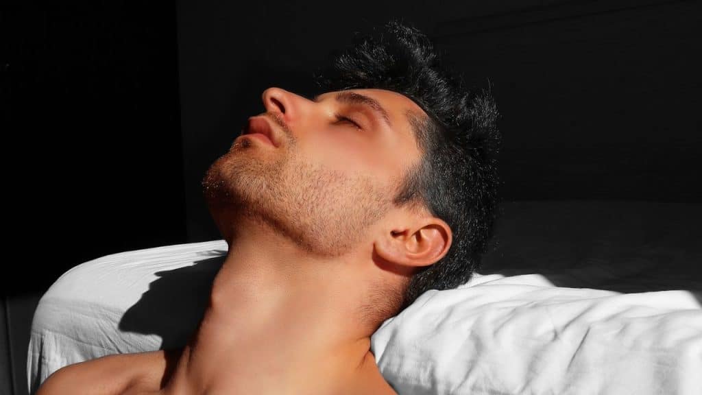 A man with his head tilted back and eyes closed is lying on a bed.