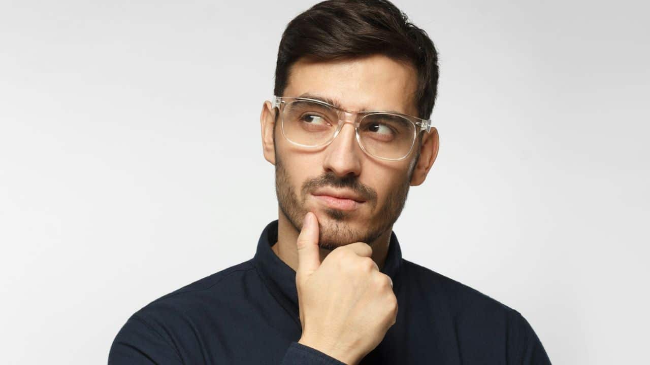 A man with glasses is looking up and to the left, with his hand on his chin in a thoughtful pose.