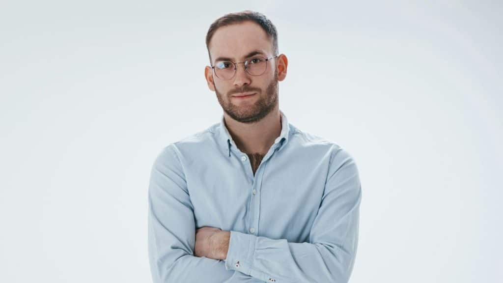 A man with glasses and a beard stands with his arms crossed, looking at the camera.