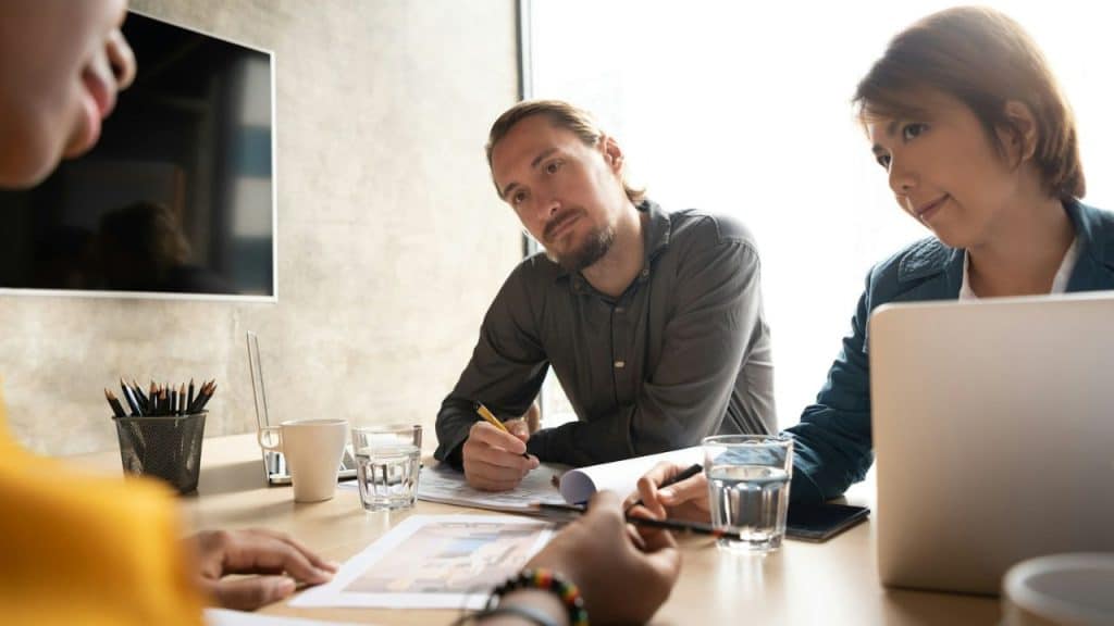 A man with a beard looks down at papers on a table during a meeting.