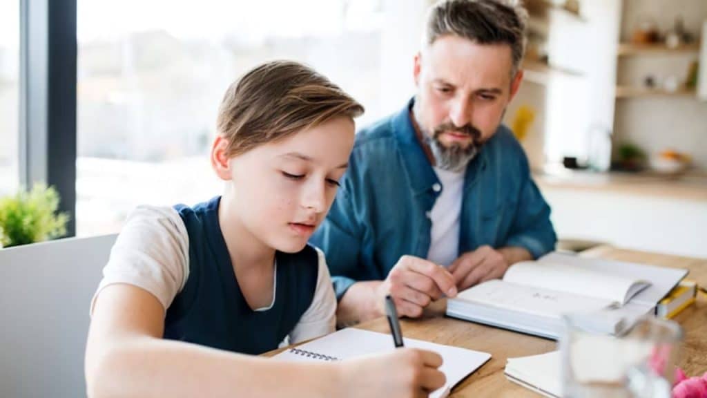 A father helping his child with homework at the kitchen table