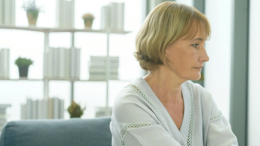 A sad, pensive middle-aged woman with blonde hair sitting and looking away.