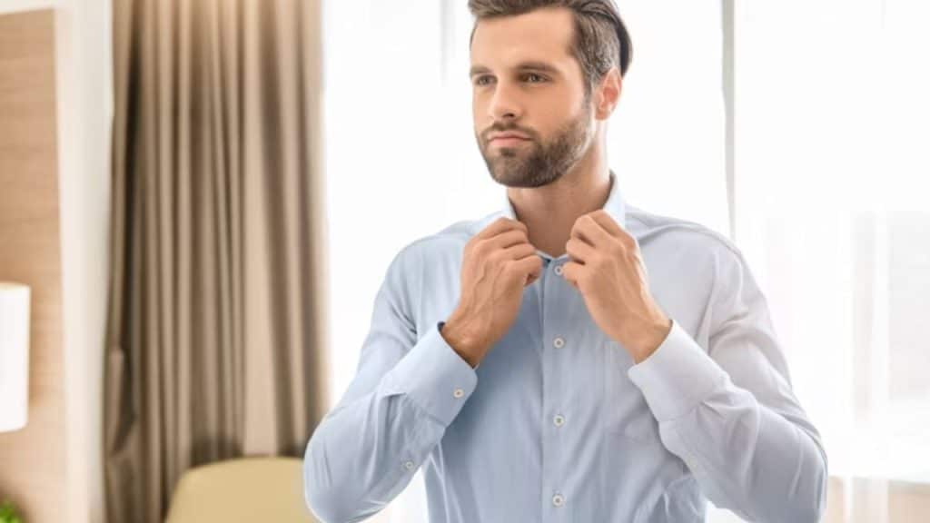 Man adjusting his shirt collar in the mirror before leaving home