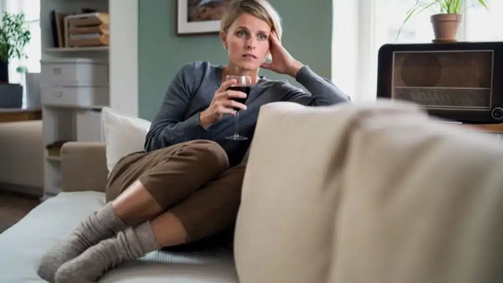 A woman sitting on a couch with a glass of wine on her hand, feeling down