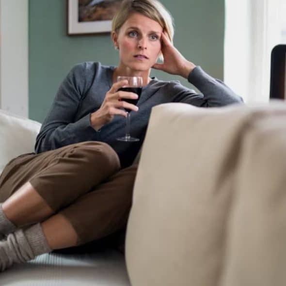 A woman sitting on a couch with a glass of wine on her hand, feeling down
