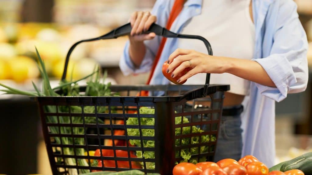 A person shops for vegetables, placing produce into a basket.