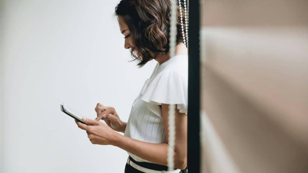 A woman in a white blouse uses a tablet while standing indoors.