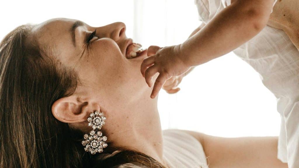 A woman wearing large earrings smiles while holding a baby who touches her face.