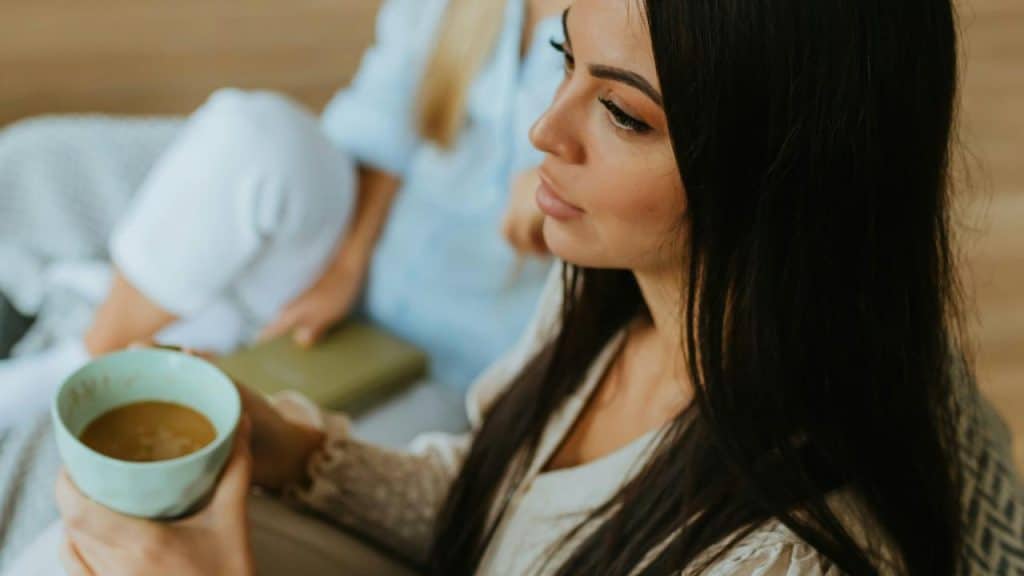 A woman with long dark hair holds a light blue mug while sitting indoors.