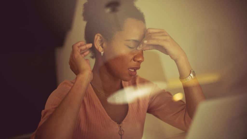A woman in a pink top holds her forehead and closes her eyes in frustration or fatigue.
