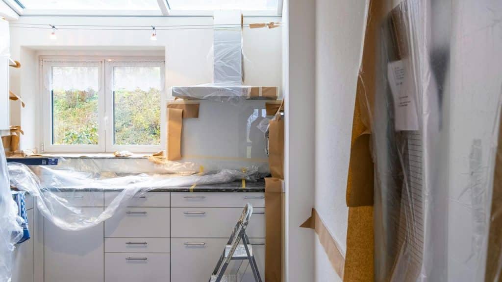 A kitchen under renovation with cabinets and appliances covered in protective plastic.