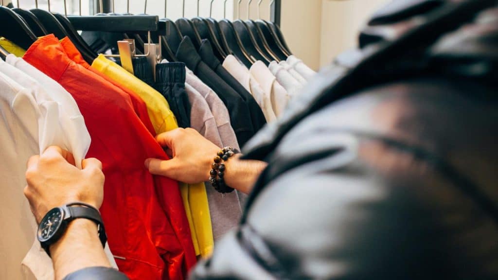A person browsing through colorful clothes on a rack.
