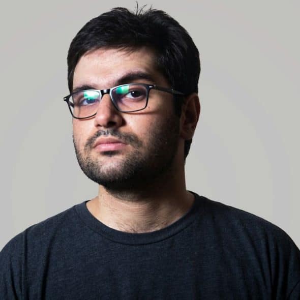 A solemn man with glasses and a beard stares at the camera.