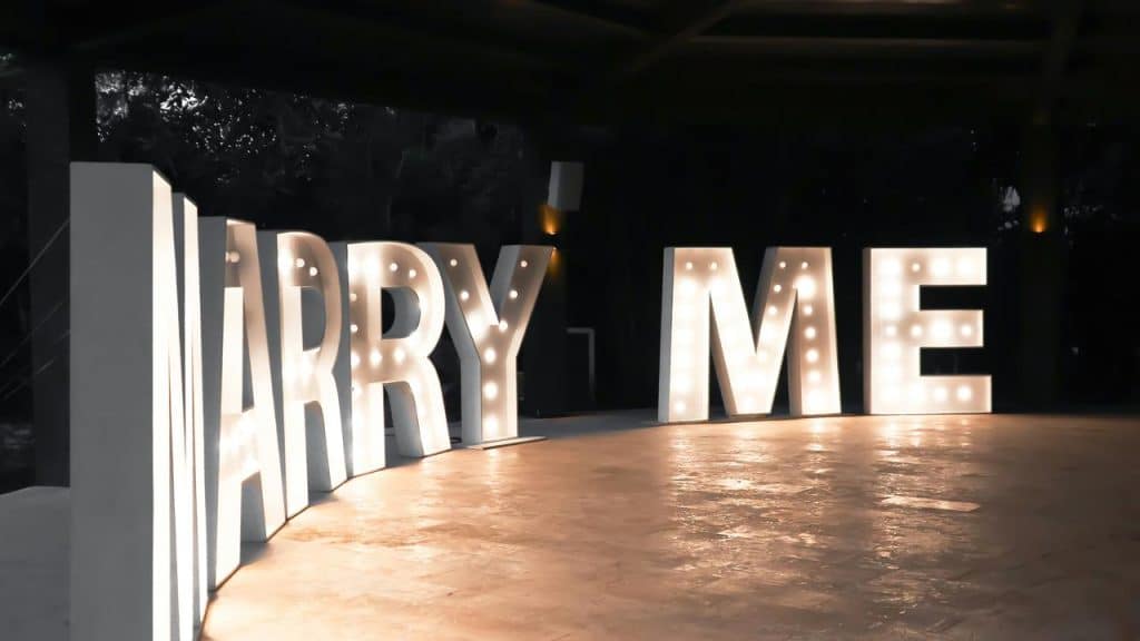 A large illuminated sign that spells out "MARRY ME" at night.
