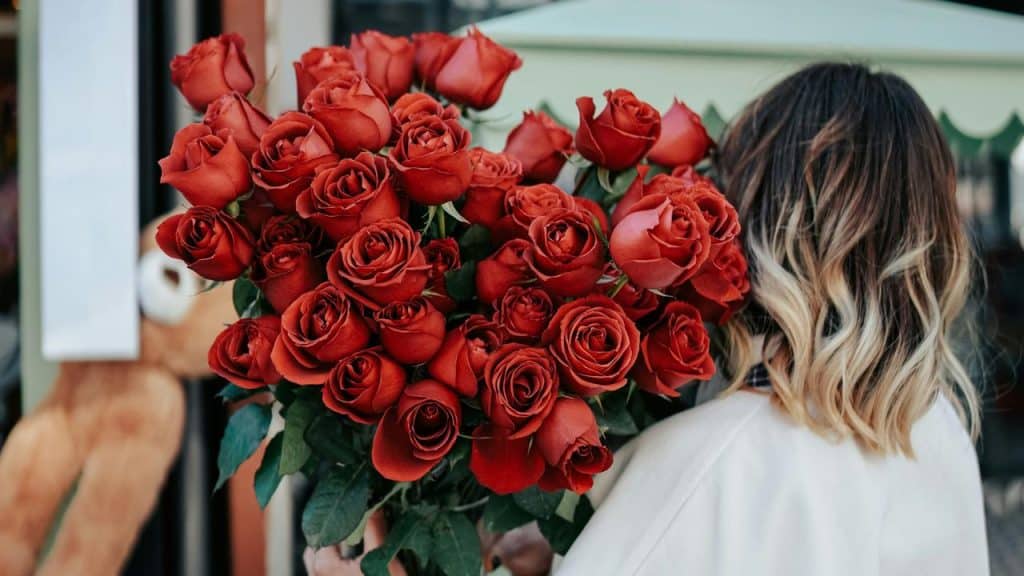 A woman holds a large bouquet of red roses.