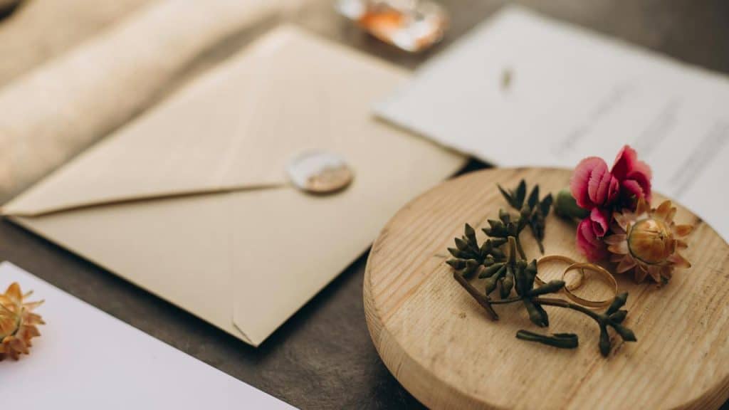 A pair of wedding rings with flowers and an envelope on a table.