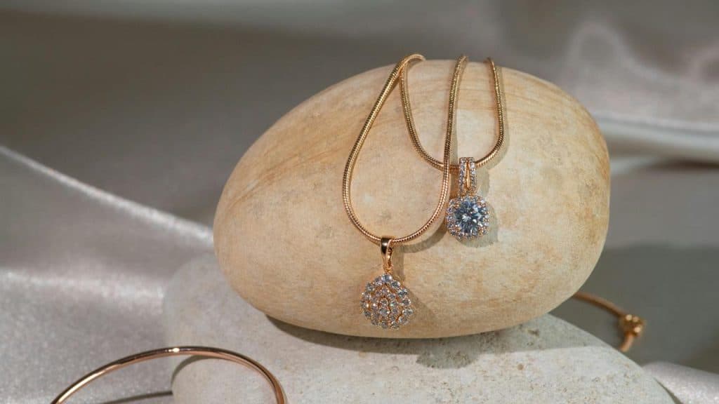A pair of gold necklaces with diamond pendants displayed on smooth stones.
