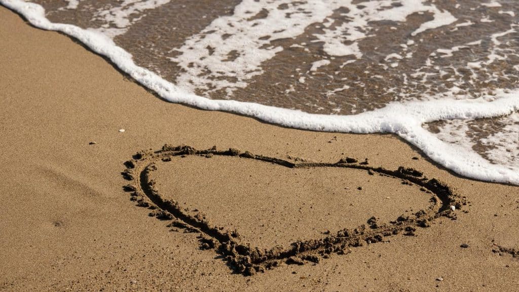 A heart drawn in the sand near the ocean waves.