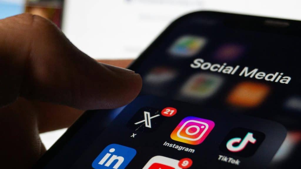 A smartphone screen shows social media apps including X, Instagram, TikTok, and LinkedIn.