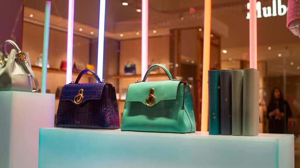 A store display showcases luxury handbags under colorful lights.