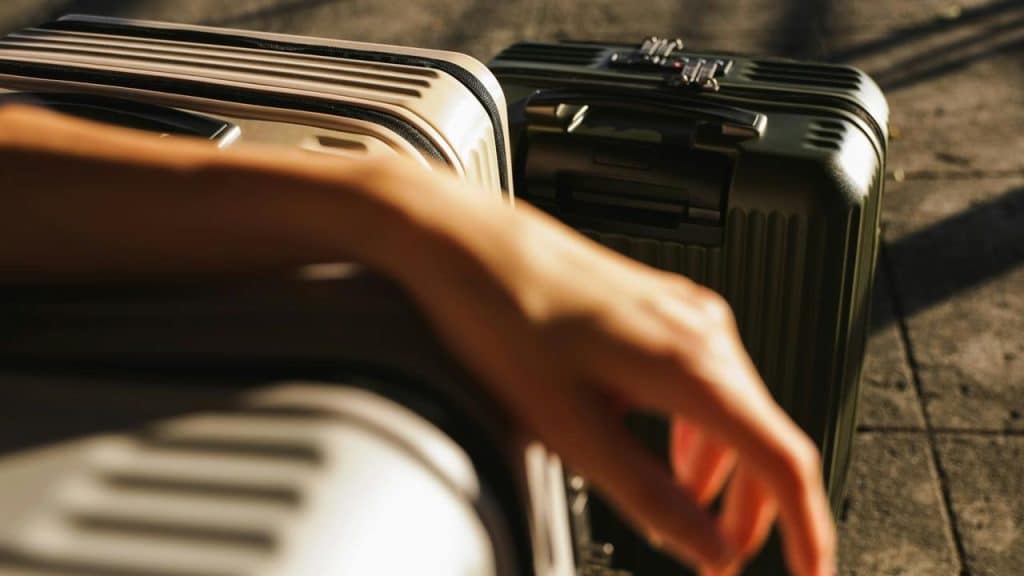 A person rests their arm on stacked suitcases in sunlight.