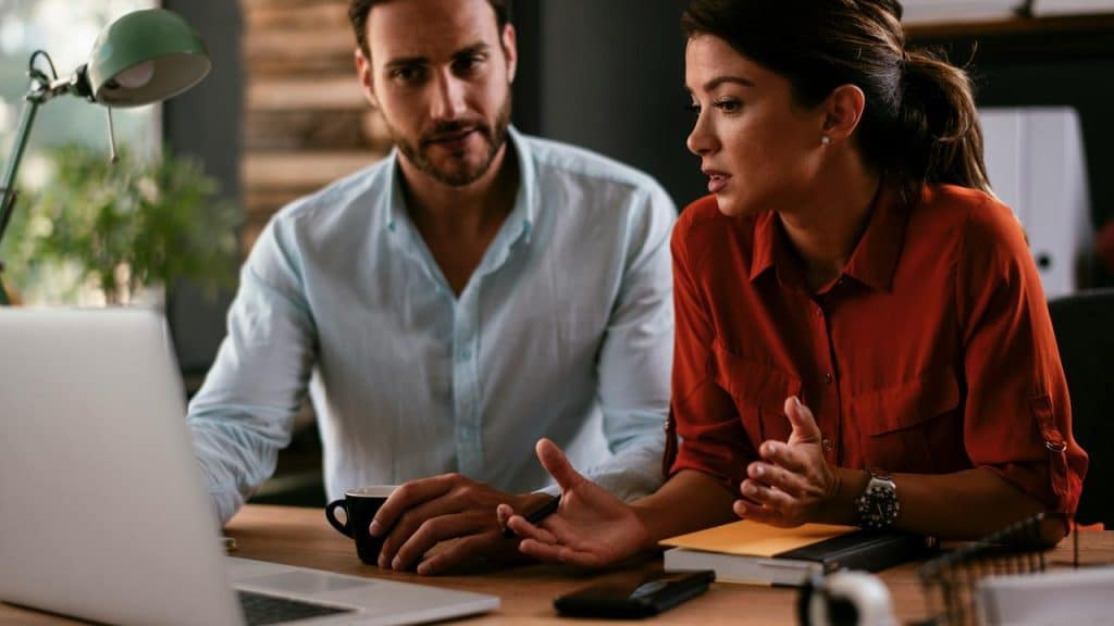 A man and woman have a serious discussion while working on a laptop.
