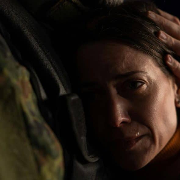 A woman with teary eyes hugs a soldier while being comforted.
