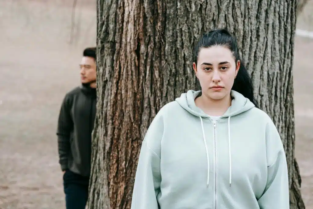 A woman in front of tree and a man behind the tree