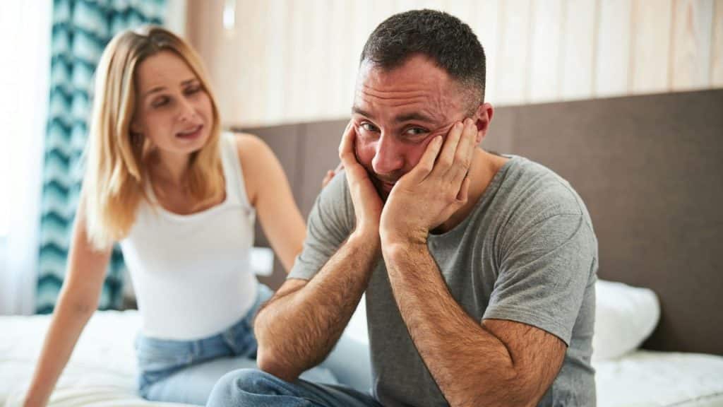 A worried woman tries to comfort a man who is holding his face in distress.