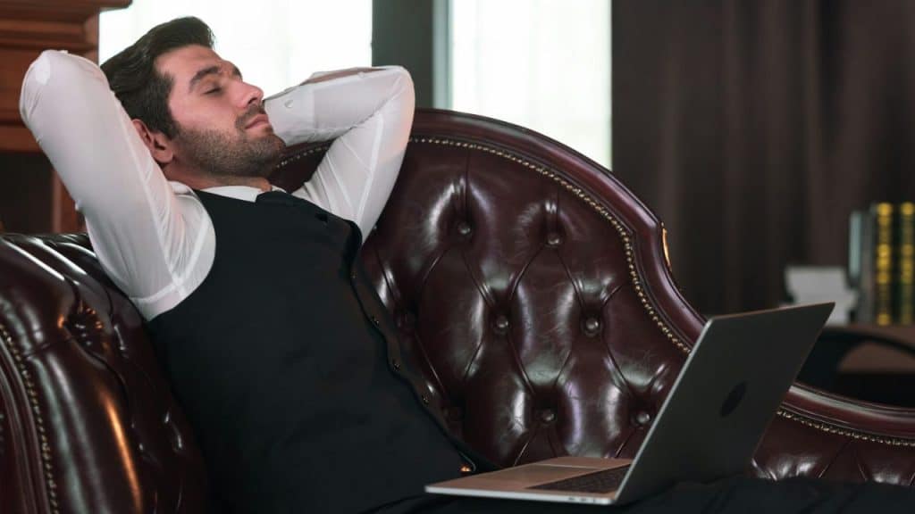 A well-dressed man relaxes on a couch with his eyes closed.