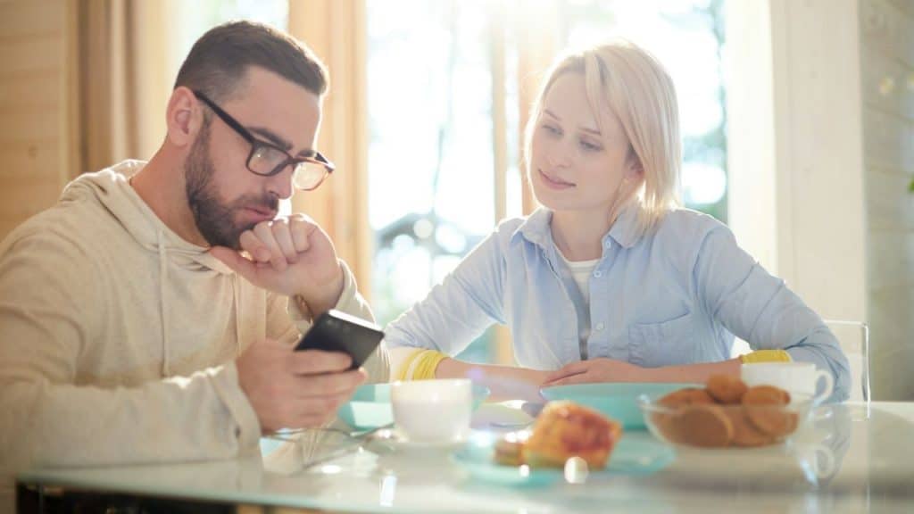 A couple sits at a table, with the man focused on his phone.