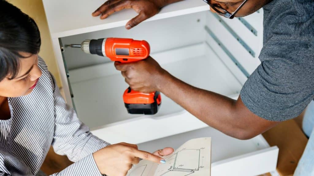 A couple works on a piece of furniture, with the woman pointing at instructions.