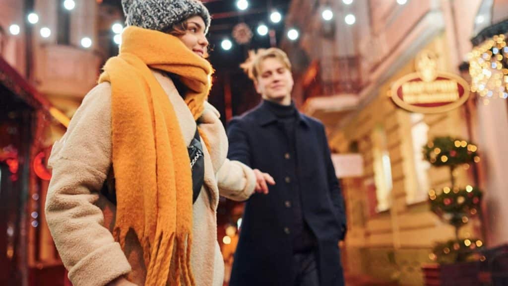 A couple walks together at night, with the woman in a beanie and scarf.