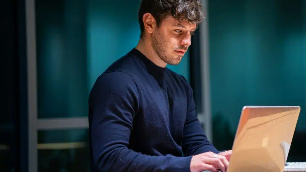 A man with a serious expression looks down at his laptop.