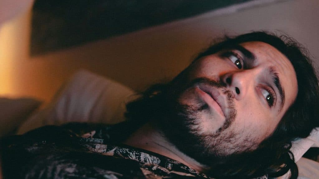 A man with a beard is lying on his back, looking off to the side.