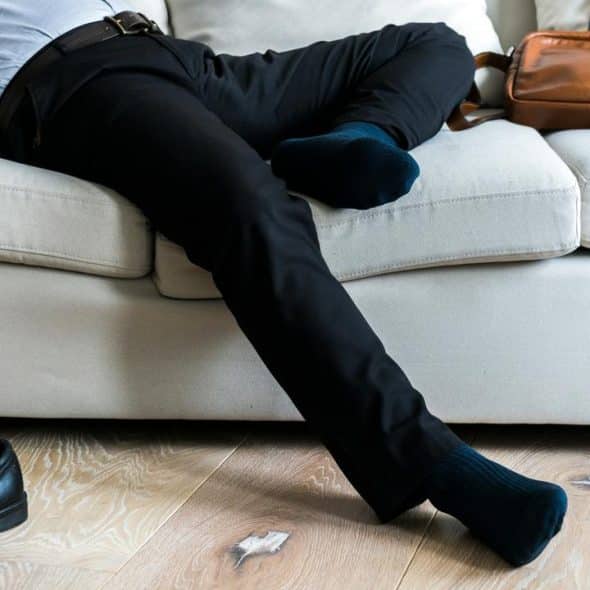 A man in business attire lying on a couch with shoes off.