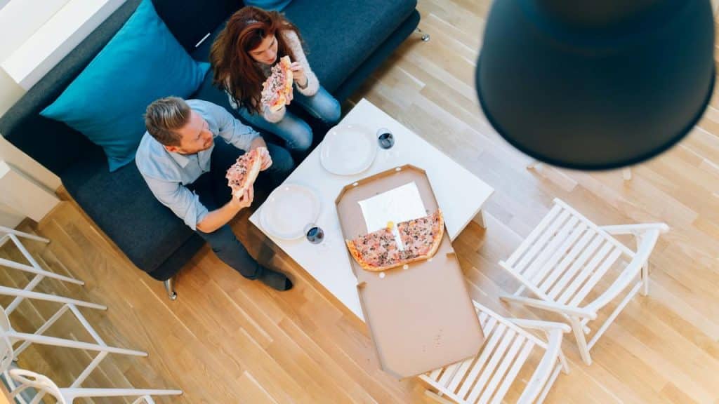A couple sitting on the floor eating pizza together.