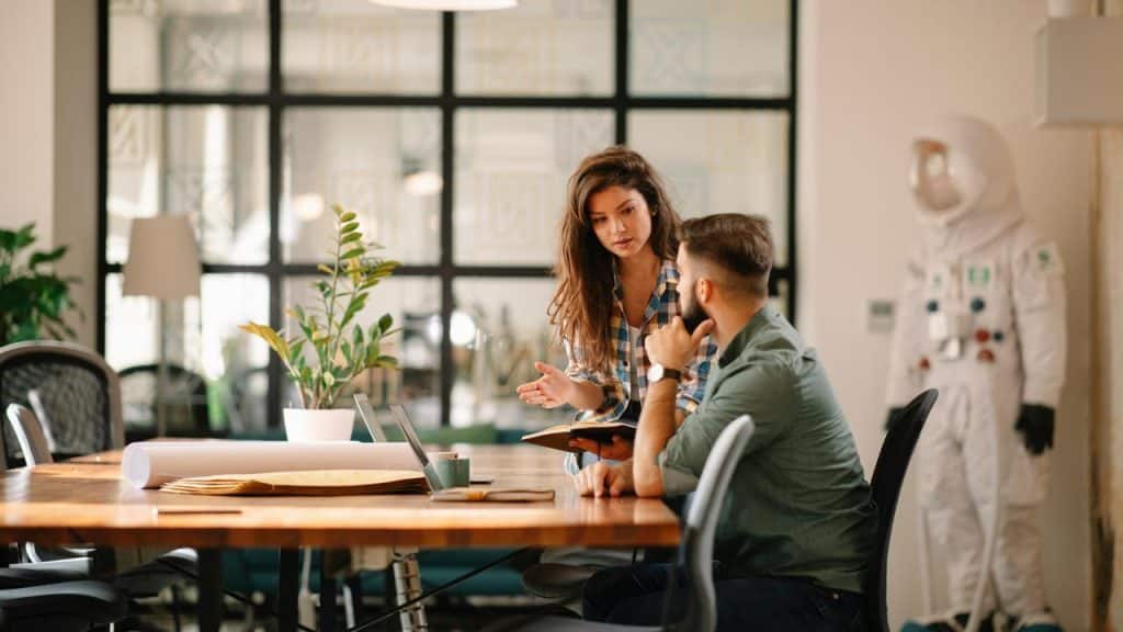 A woman talking to a man while working together at a desk.