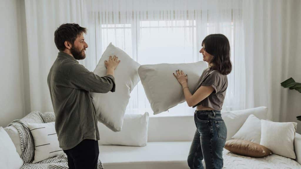 A couple playfully holding pillows facing each other.