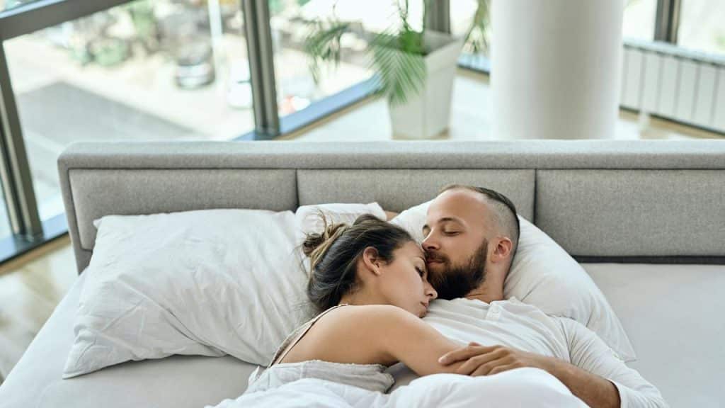 A couple lying in bed cuddling peacefully.
