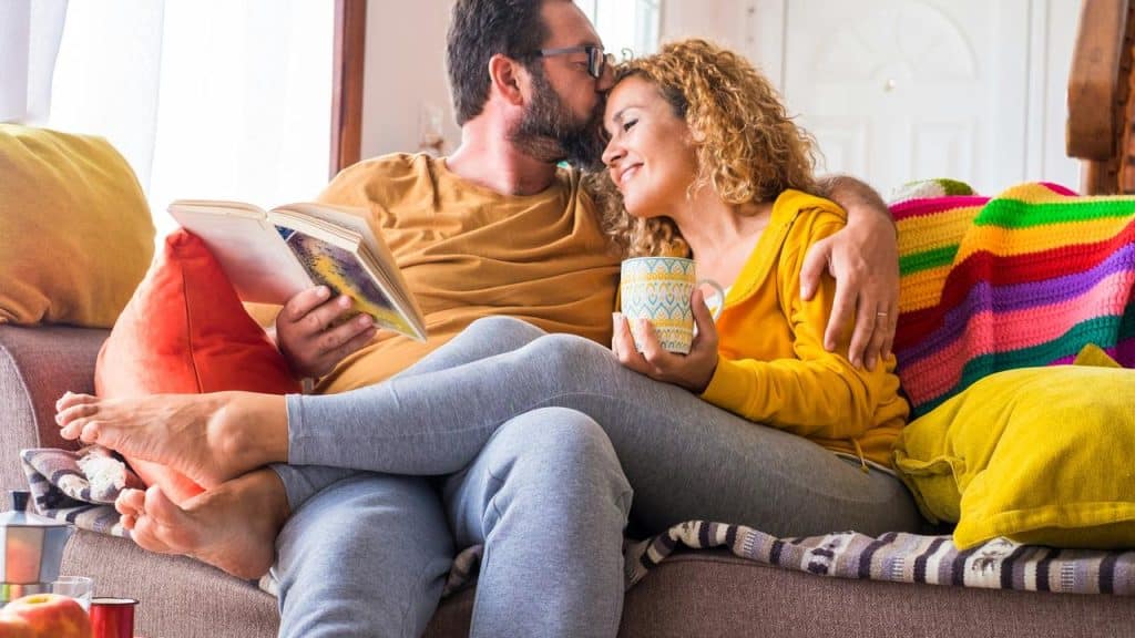 A couple cuddling on a couch while reading and drinking coffee.