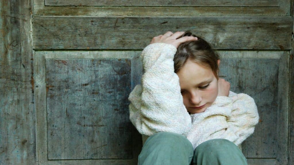 A child looking sad in front of the door